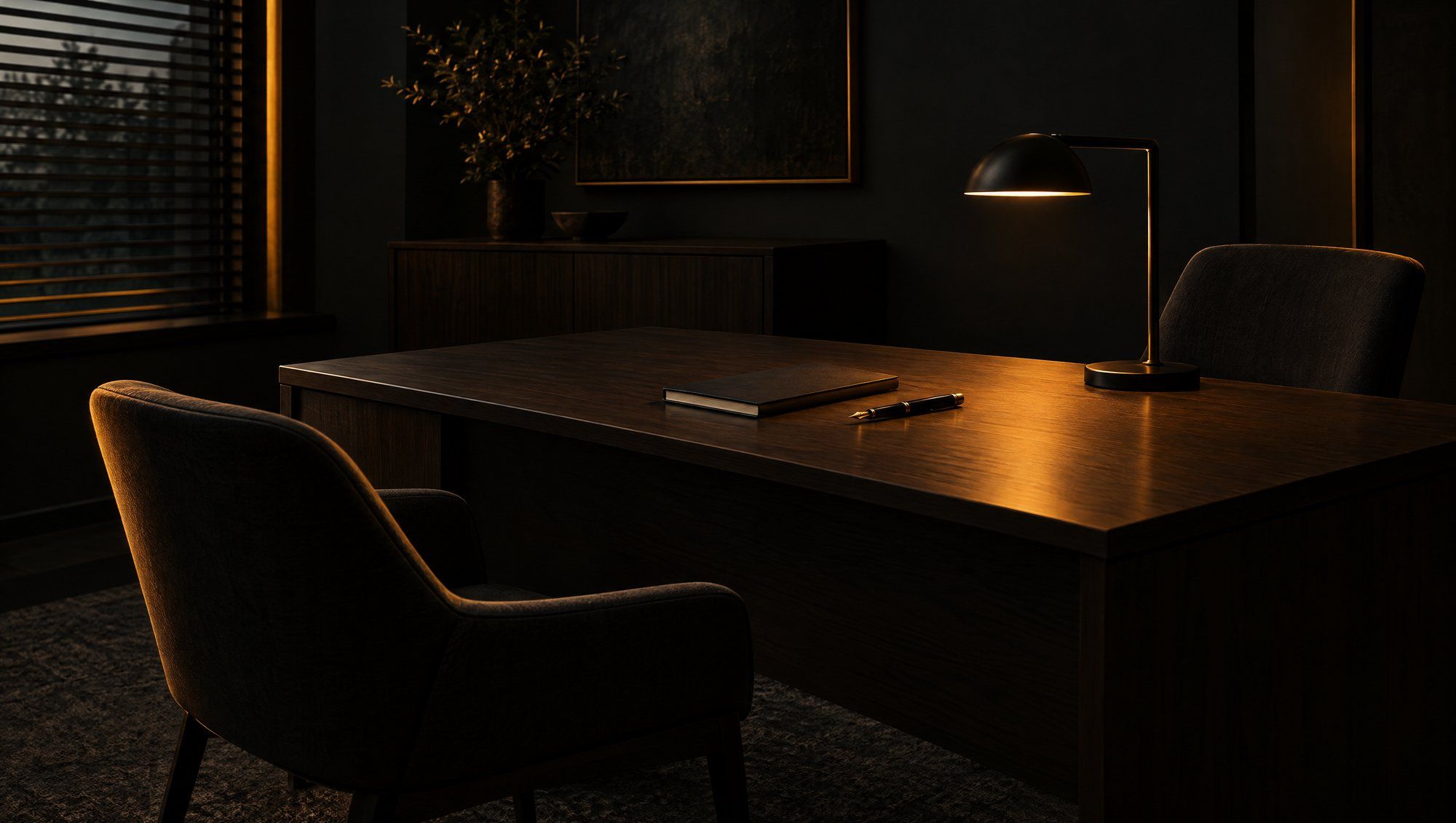 An empty office with a wooden desk, a closed notebook, a pen, two chairs and a lit desk lamp