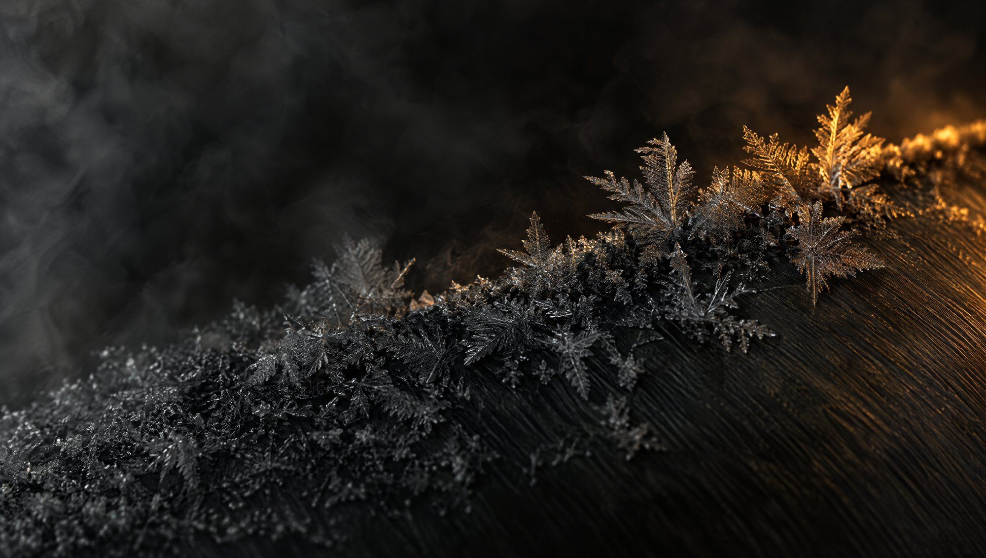 Close-up of frost crystals forming on a dark metal surface, one edge lit in warm light