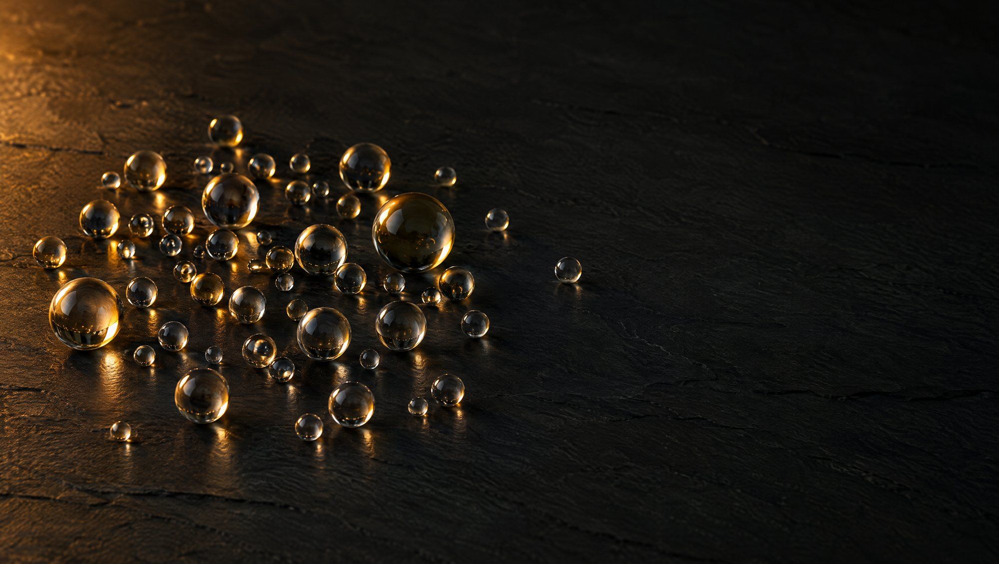 Dozens of small clear glass spheres clustered on a dark slate surface, a few catching warm amber light